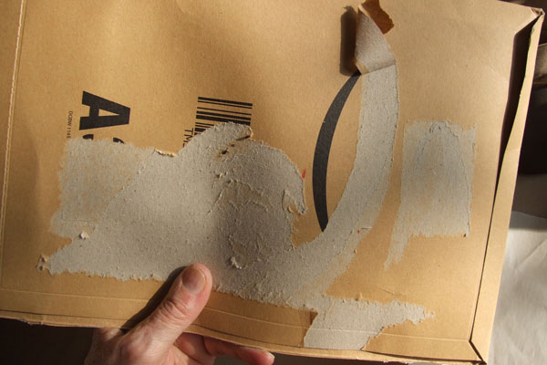 The surface layer of cardboard is peeled away as labels are removed.